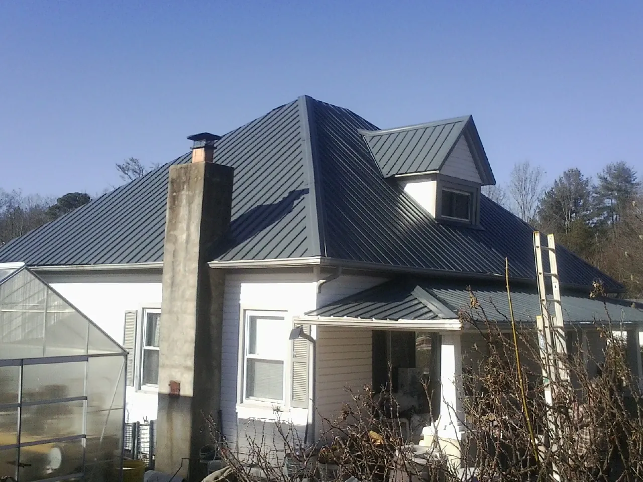 Dark blue standing seam metal roof on a white farmhouse with dormer — Slate & Tile Roof Repair by Roofing Brothers in Little Chute