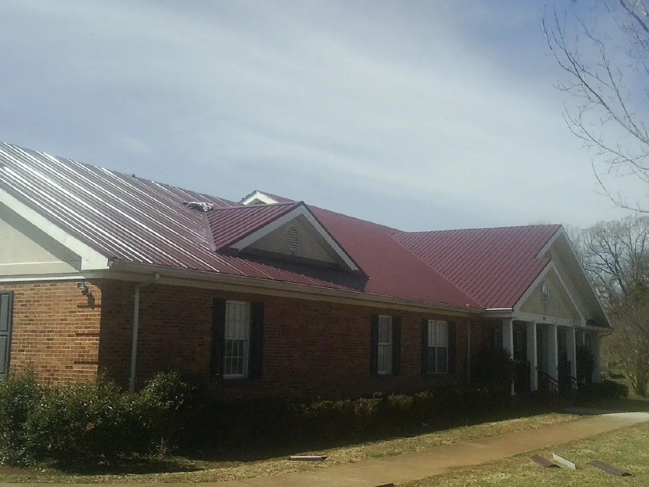 Red metal roof with gabled entries on a long brick building, from a Hail Damage Roof Repair job in Little Chute