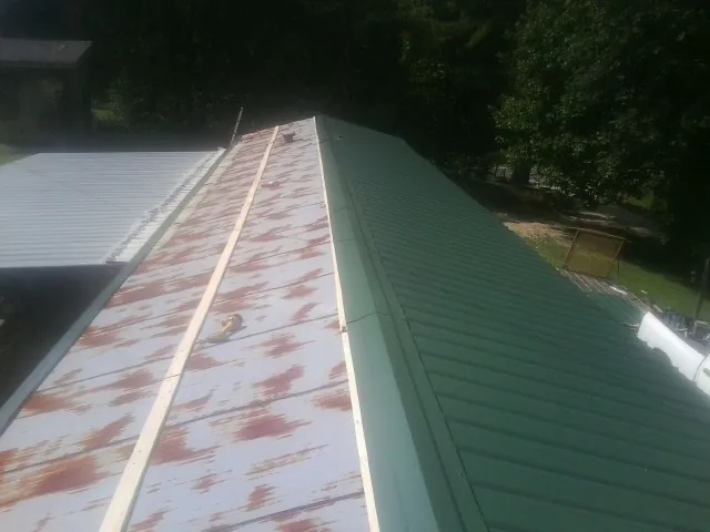 Old rusted panels beside newly installed green metal roofing — Wind Damage Roof Repair by Roofing Brothers in Little Chute