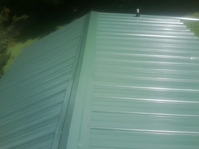 New green metal panels meeting at the ridge of a roof — Flat Roof Repair work by our crew in Little Chute