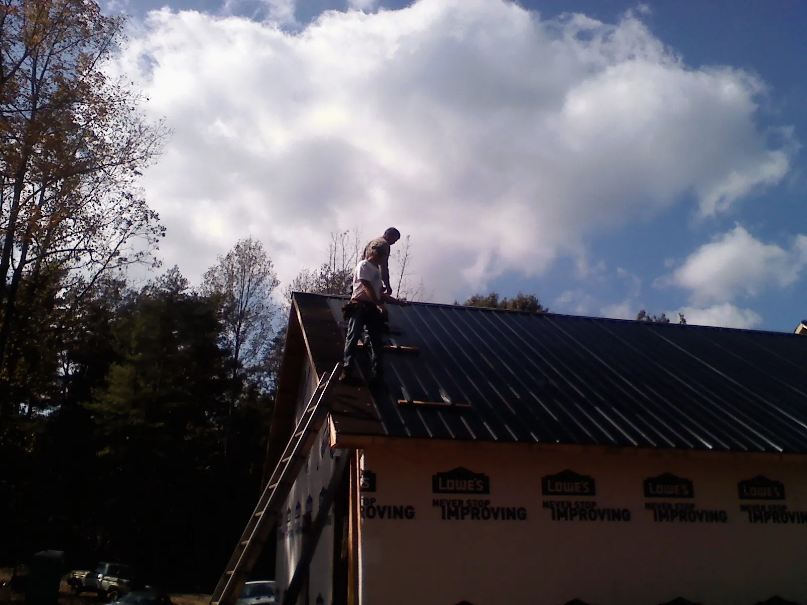 Roofer fastening dark metal panels high against a cloudy sky, from a Roof Inspection job in Little Chute