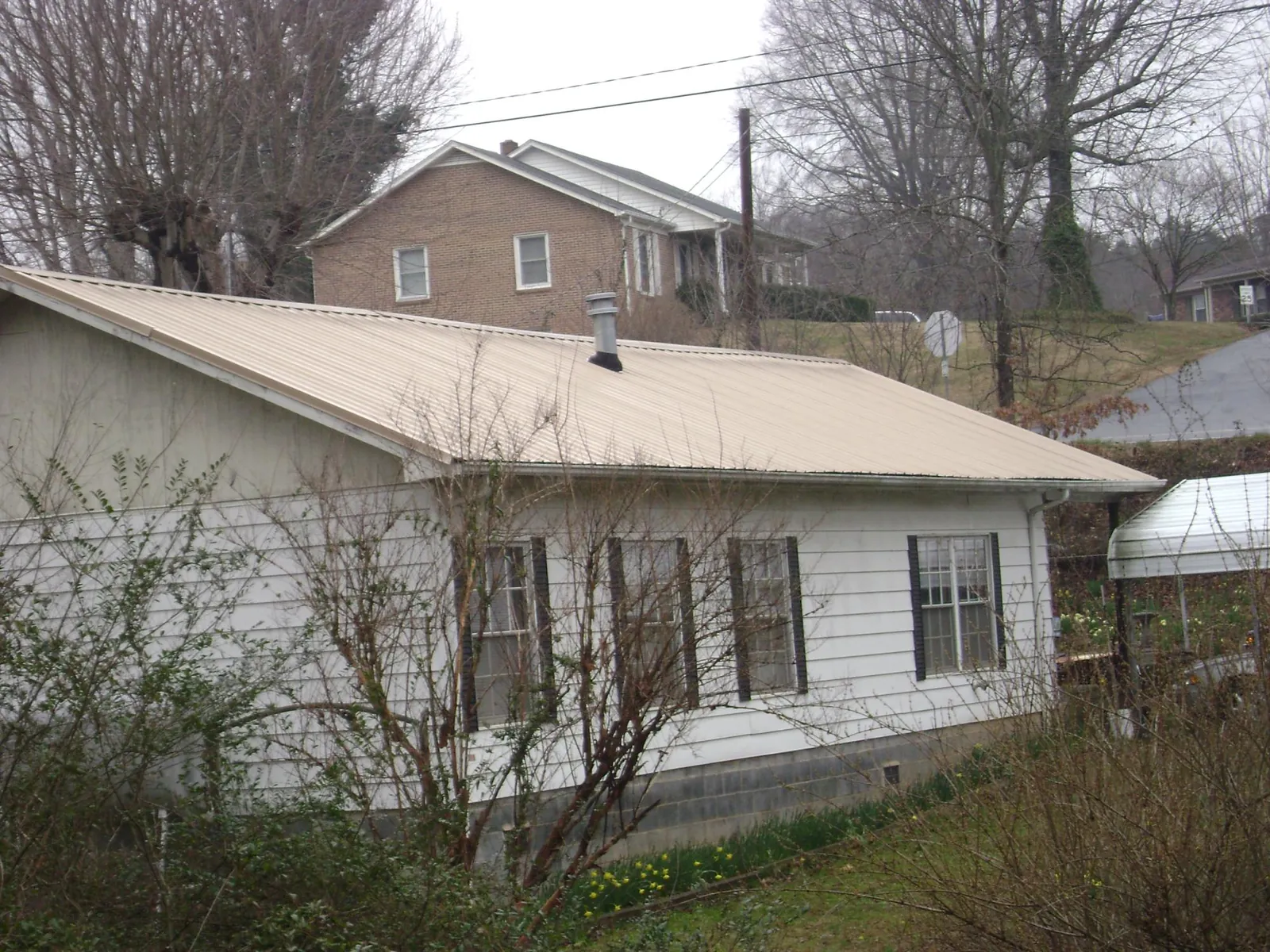 Tan metal roof on a white sided house set into a hillside — Commercial Roofing by Roofing Brothers in Little Chute